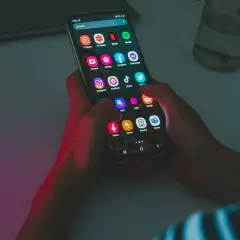 Dłonie trzymają smartfon z ikonami aplikacji, w tym Instagram i TikTok. Wskazówka do oszczędzania baterii: wyłącz niepotrzebne aplikacje.