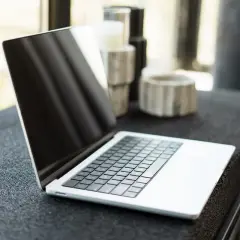Nowy laptop czeka na pierwsze uruchomienie komputera. Na blacie obok ozdobne wazony.