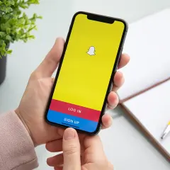 Dłoń trzyma smartfon z ekranem logowania Snapchata. Chcesz wiedzieć, jak usunąć story na Snapie?