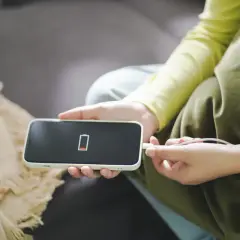 Dramatyczny spadek baterii przez noc na iPhonie. Czerwony wskaźnik pokazuje prawie zerowy poziom naładowania, a użytkownik podłącza ładowarkę.
