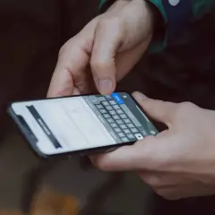 Dłonie trzymające smartfon, na ekranie klawiatura. Dowiedz się, jak zmienić czcionkę w telefonie, aby spersonalizować wygląd.