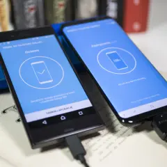 Dwa telefony połączone kablem USB. Jeden z nich pokazuje komunikat "Gotowe", drugi "100% Aktualizacja danych Kontakty...", co jest częścią procesu jak uruchomić nowy telefon Samsung.