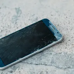 Rozbity ekran telefonu Samsung z widoczną pękniętą kreską na wyświetlaczu, leżący na betonowej powierzchni.