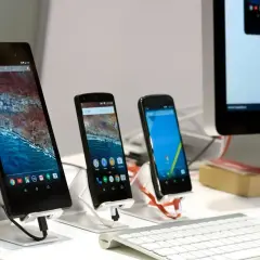 Na biurku stoją trzy smartfony i tablet, a obok klawiatura i monitor komputera. Można wysłać sms na komputerze.