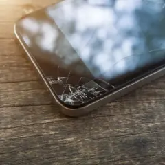 Zbity ekran telefonu leży na drewnianym blacie. Pęknięcia tworzą pajęczynę na szkle, świadcząc o niefortunnym upadku.