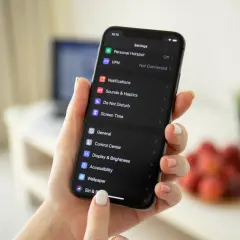 Dłoń trzyma iPhone'a z ciemnym motywem. Na ekranie widać ustawienia, w tym opcję "Wallpaper", która pomoże Ci dowiedzieć się, jak zmienić motyw na IG.