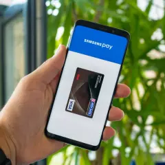 Dłoń trzyma smartfon z otwartą aplikacją Samsung Wallet, na ekranie widoczna karta płatnicza Visa.