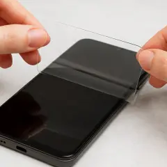 Dłonie delikatnie odklejają folię ochronną od ekranu telefonu. Dowiedz się, jak zdjąć szkło hartowane z telefonu, by zrobić to bezpiecznie.
