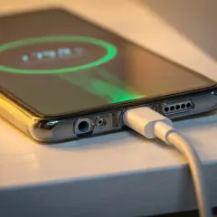 Zbliżenie na telefon w przezroczystym etui, podłączony do ładowania. Na ekranie widoczny wskaźnik baterii 79%.