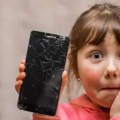 Zaskoczona dziewczynka pokazuje pęknięty ekran telefonu. Czy da się usunąć rysy ze szkła hartowanego?