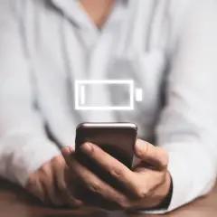 Osoba trzyma smartfon z ikoną niskiego poziomu baterii. Dowiedz się, jak wyłączyć optymalizację baterii Samsung, by dłużej cieszyć się energią.