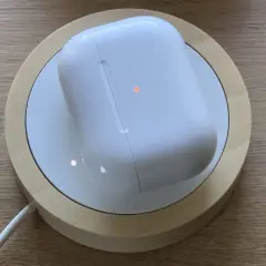 Białe etui AirPods na ładowarce bezprzewodowej, z pomarańczową diodą. Dowiedz się, jak czyscic airpods, by wyglądały jak nowe.