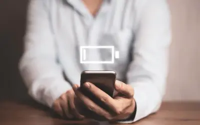 Osoba trzyma smartfon z ikoną niskiego poziomu baterii. Dowiedz się, jak wyłączyć optymalizację baterii Samsung, by dłużej cieszyć się energią.