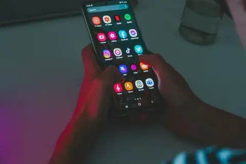 Dłonie trzymają smartfon z ikonami aplikacji, w tym Instagram i TikTok. Wskazówka do oszczędzania baterii: wyłącz niepotrzebne aplikacje.