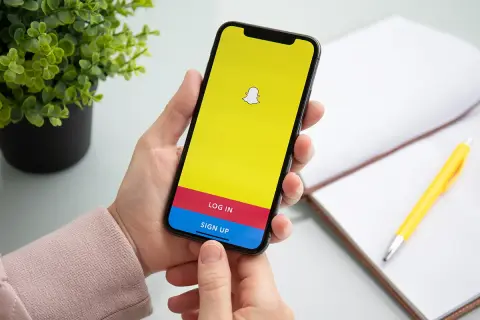 Dłoń trzyma smartfon z ekranem logowania Snapchata. Chcesz wiedzieć, jak usunąć story na Snapie?