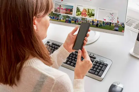 Kobieta trzyma smartfon, przygotowując podłączenie telefonu do monitora. Na ekranie widać zdjęcia z wydarzenia.