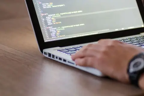 Dłoń programisty pisze kod na laptopie, co może być częścią procesu, jak sprawdzić wydajność laptopa.
