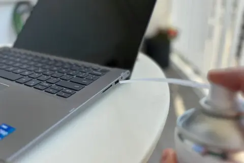 Czyszczenie laptopa z kurzu sprężonym powietrzem. Dmuchawa wylatuje z puszki w kierunku szczeliny obok klawiatury.
