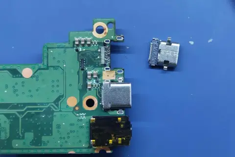 Luźne gniazdo USB C obok płyty głównej. Naprawa laptopa wymaga precyzji.