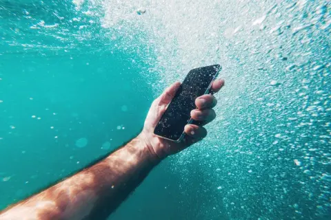 Dłoń trzyma smartfon pod wodą, pokazując jego wodoszczelność IP52. Bąbelki powietrza unoszą się wokół.
