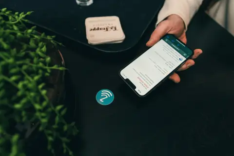 Dłoń trzyma smartfon z menu restauracji, obok symbol NFC. To pokazuje, jak działa NFC, co to jest i jak ułatwia płatności.