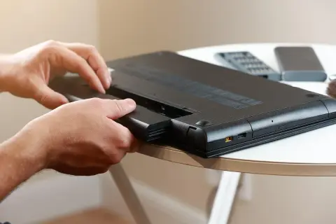 Dłonie wyjmują baterię z laptopa. Dowiedz się, jak sprawdzić kondycję baterii w laptopie, by cieszyć się dłuższym czasem pracy.
