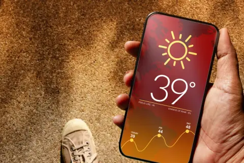 Dłoń trzyma telefon z prognozą pogody: 39 stopni, upał. Czy to już throttling?