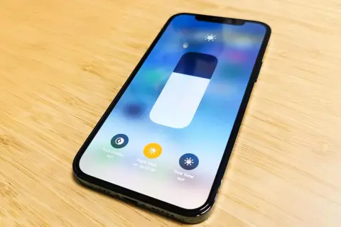 Na ekranie iPhone'a widać suwak jasności i opcje: Tryb ciemny, Night Shift i True Tone. Dowiedz się, jak zmienic kolor godziny w iPhone.
