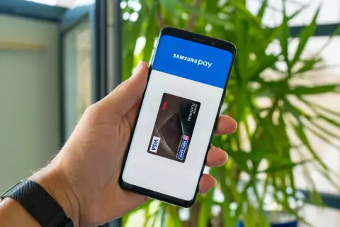 Dłoń trzyma smartfon z otwartą aplikacją Samsung Wallet, na ekranie widoczna karta płatnicza Visa.