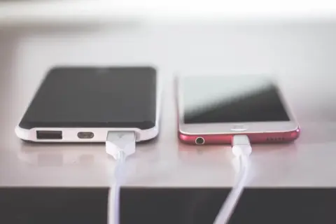 Dwa telefony podłączone do ładowania. Jeden z nich ma zepsute gniazdo ładowania w telefonie, co uniemożliwia mu pobieranie energii.