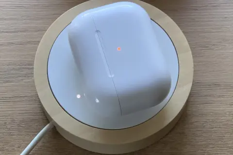 Białe etui AirPods na ładowarce bezprzewodowej, z pomarańczową diodą. Dowiedz się, jak czyscic airpods, by wyglądały jak nowe.