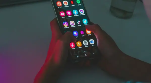 Dłonie trzymają smartfon z ikonami aplikacji, w tym Instagram i TikTok. Wskazówka do oszczędzania baterii: wyłącz niepotrzebne aplikacje.