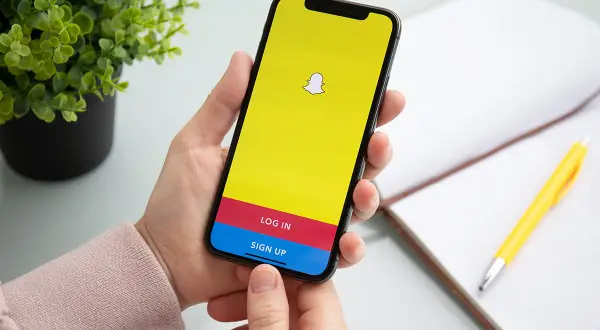 Dłoń trzyma smartfon z ekranem logowania Snapchata. Chcesz wiedzieć, jak usunąć story na Snapie?