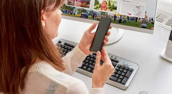 Kobieta trzyma smartfon, przygotowując podłączenie telefonu do monitora. Na ekranie widać zdjęcia z wydarzenia.