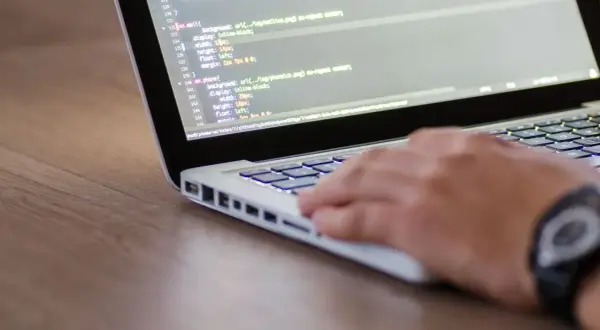 Dłoń programisty pisze kod na laptopie, co może być częścią procesu, jak sprawdzić wydajność laptopa.