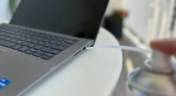 Czyszczenie laptopa z kurzu sprężonym powietrzem. Dmuchawa wylatuje z puszki w kierunku szczeliny obok klawiatury.