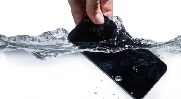 Dłoń wyciąga czarny telefon z wody. Zastanawiasz się, jak wysuszyć telefon po zalaniu?
