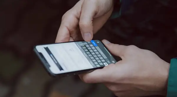 Dłonie trzymające smartfon, na ekranie klawiatura. Dowiedz się, jak zmienić czcionkę w telefonie, aby spersonalizować wygląd.