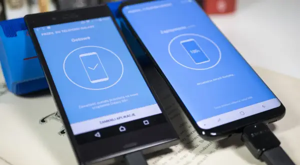 Dwa telefony połączone kablem USB. Jeden z nich pokazuje komunikat "Gotowe", drugi "100% Aktualizacja danych Kontakty...", co jest częścią procesu jak uruchomić nowy telefon Samsung.
