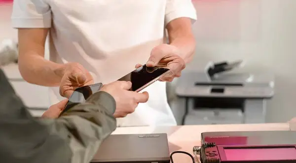 Pracownik serwisu pomaga w usuwaniu danych z telefonu, przekazując go klientowi.