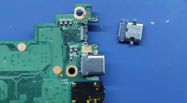 Luźne gniazdo USB C obok płyty głównej. Naprawa laptopa wymaga precyzji.