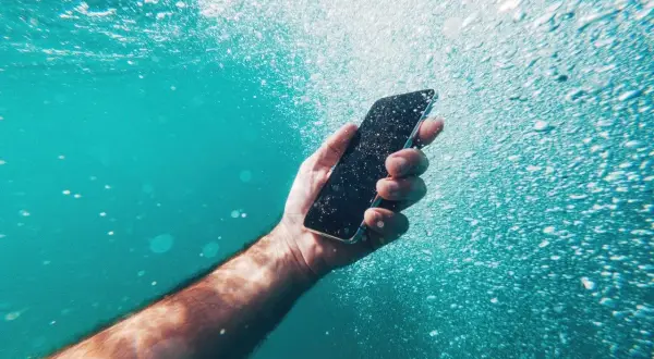Dłoń trzyma smartfon pod wodą, pokazując jego wodoszczelność IP52. Bąbelki powietrza unoszą się wokół.