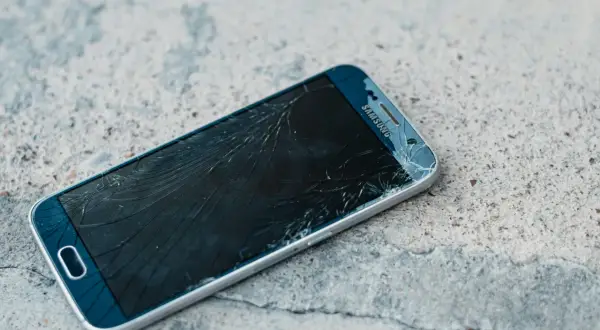 Rozbity ekran telefonu Samsung z widoczną pękniętą kreską na wyświetlaczu, leżący na betonowej powierzchni.