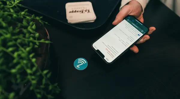 Dłoń trzyma smartfon z menu restauracji, obok symbol NFC. To pokazuje, jak działa NFC, co to jest i jak ułatwia płatności.