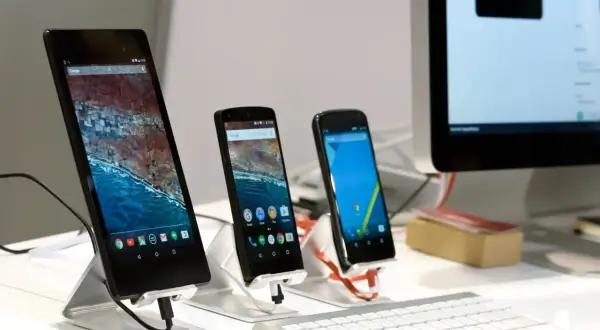 Na biurku stoją trzy smartfony i tablet, a obok klawiatura i monitor komputera. Można wysłać sms na komputerze.