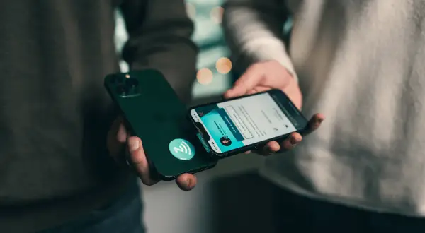 Dwie osoby zbliżają do siebie iPhone'y, jeden z nich ma naklejkę z symbolem NFC.