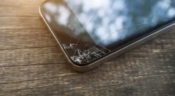 Zbity ekran telefonu leży na drewnianym blacie. Pęknięcia tworzą pajęczynę na szkle, świadcząc o niefortunnym upadku.