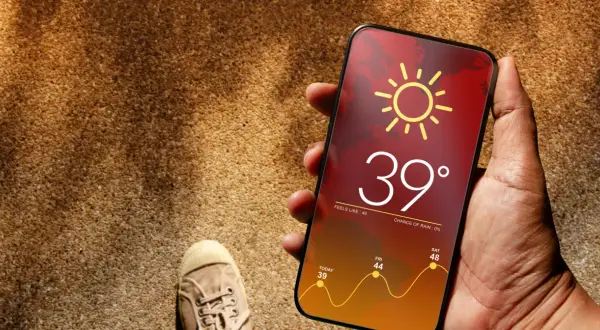 Dłoń trzyma telefon z prognozą pogody: 39 stopni, upał. Czy to już throttling?