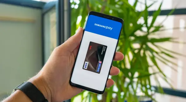 Dłoń trzyma smartfon z otwartą aplikacją Samsung Wallet, na ekranie widoczna karta płatnicza Visa.