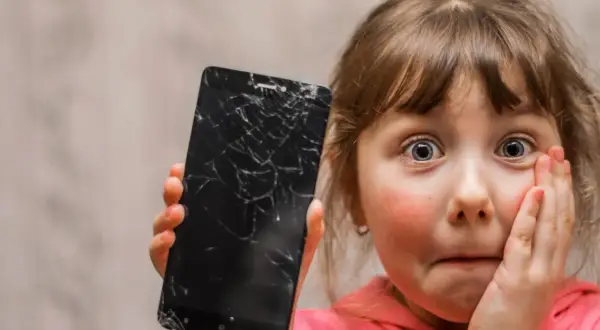 Zaskoczona dziewczynka pokazuje pęknięty ekran telefonu. Czy da się usunąć rysy ze szkła hartowanego?